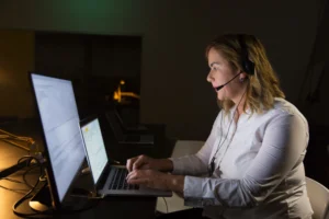 Agentes de IA Autônomos: Como Estão Mudando o Atendimento ao Cliente em 2026: Atendente em call center com headset usando notebook e monitor durante atendimento ao cliente em ambiente de escritório, com foco em automação e suporte digital.