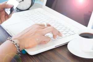 Backup: Por Que Empresas Precisam Ter Uma Estratégia Para Proteger Seus Arquivos — pessoa digitando em notebook e segurando um cartão, sugerindo transferência e cópia de dados para segurança das informações